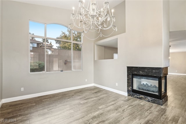 unfurnished living room featuring a fireplace, wood-type flooring, a towering ceiling, and a notable chandelier