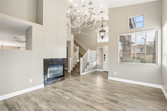 unfurnished living room featuring a premium fireplace, ceiling fan with notable chandelier, wood-type flooring, and a high ceiling