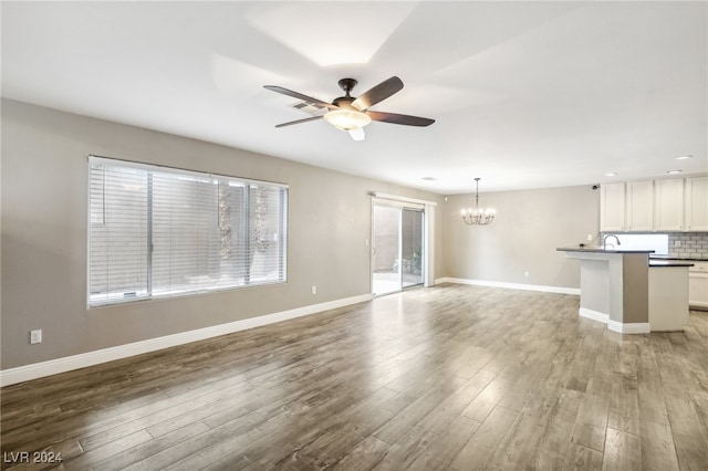 unfurnished living room featuring hardwood / wood-style floors and ceiling fan with notable chandelier