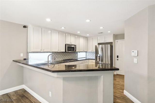 kitchen with kitchen peninsula, stainless steel appliances, white cabinetry, and dark hardwood / wood-style floors