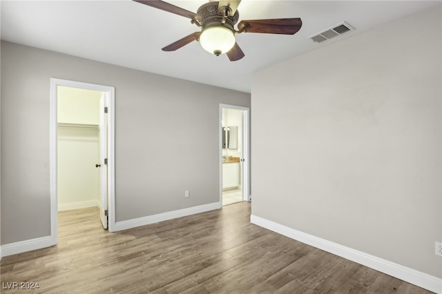 unfurnished bedroom featuring light wood-type flooring, ensuite bath, ceiling fan, a spacious closet, and a closet