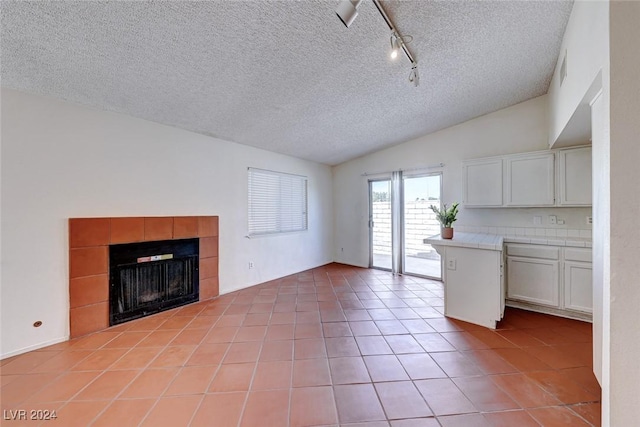 unfurnished living room with light tile patterned floors, lofted ceiling, a tile fireplace, rail lighting, and a textured ceiling