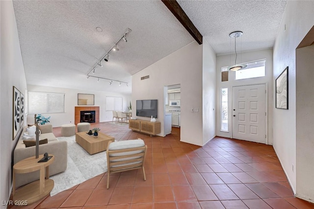 tiled living room featuring high vaulted ceiling, beam ceiling, track lighting, a textured ceiling, and a tiled fireplace