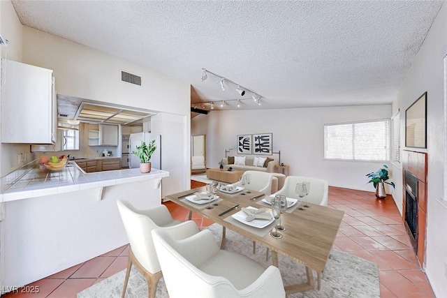 dining area with a tiled fireplace, light tile patterned floors, visible vents, and a textured ceiling