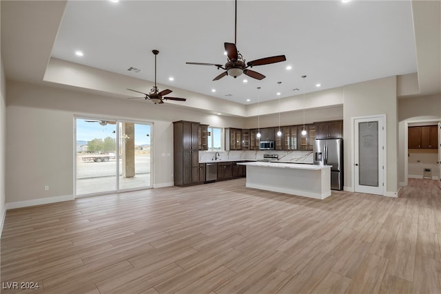 kitchen featuring hanging light fixtures, light wood-type flooring, appliances with stainless steel finishes, a kitchen island, and dark brown cabinetry