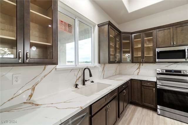 kitchen with appliances with stainless steel finishes, tasteful backsplash, light stone counters, sink, and light hardwood / wood-style floors