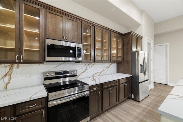 kitchen featuring light stone counters, backsplash, appliances with stainless steel finishes, and light hardwood / wood-style flooring