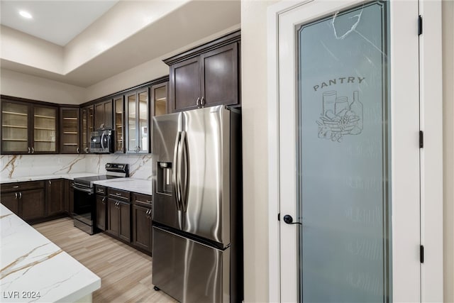 kitchen with dark brown cabinetry, light stone counters, backsplash, light hardwood / wood-style floors, and appliances with stainless steel finishes