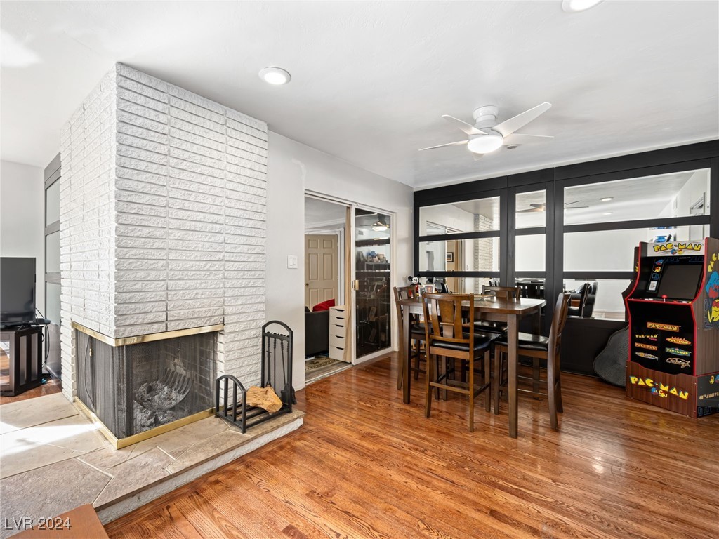 dining space with hardwood / wood-style floors, ceiling fan, and a brick fireplace