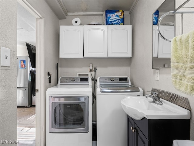 washroom with cabinets, crown molding, washer and dryer, and sink