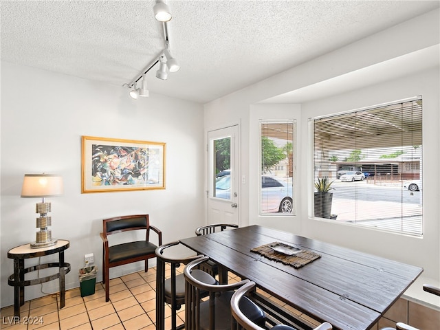 dining space featuring rail lighting, a healthy amount of sunlight, light tile patterned floors, and a textured ceiling