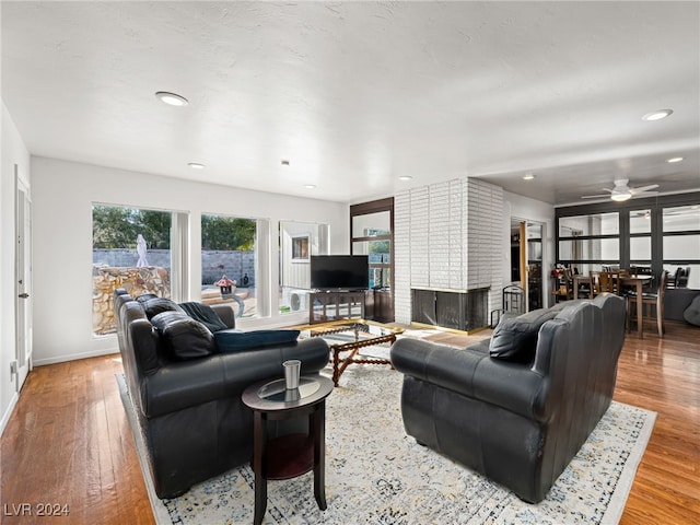 living room featuring ceiling fan, light hardwood / wood-style floors, and a brick fireplace