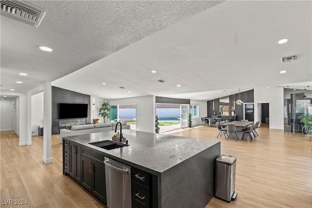 kitchen featuring sink, dishwasher, a textured ceiling, a kitchen island with sink, and light wood-type flooring