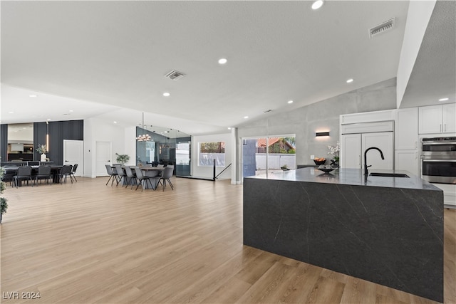 living room featuring light wood-type flooring, high vaulted ceiling, a notable chandelier, and sink