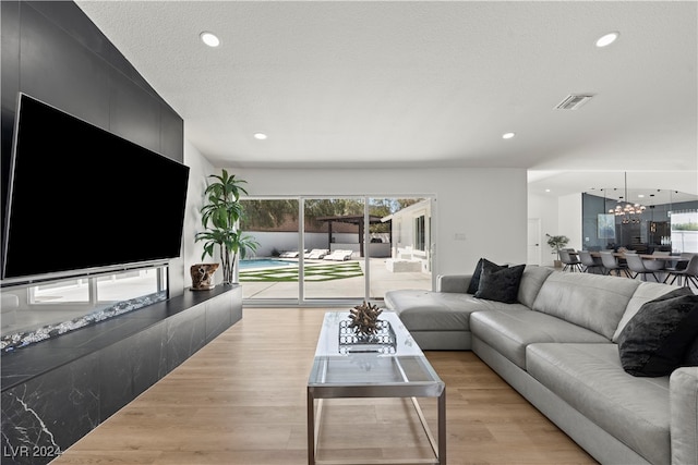 living room featuring a chandelier, a textured ceiling, and light wood-type flooring