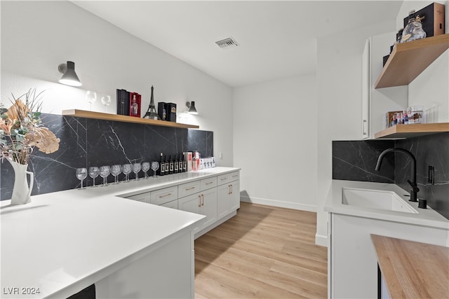 kitchen with backsplash, sink, white cabinets, and light hardwood / wood-style flooring