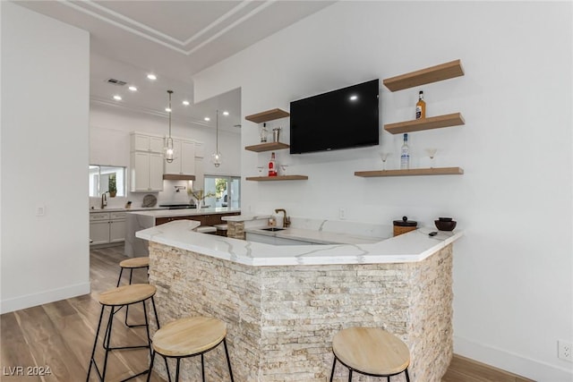 bar featuring sink, white cabinets, light stone counters, light wood-type flooring, and pendant lighting