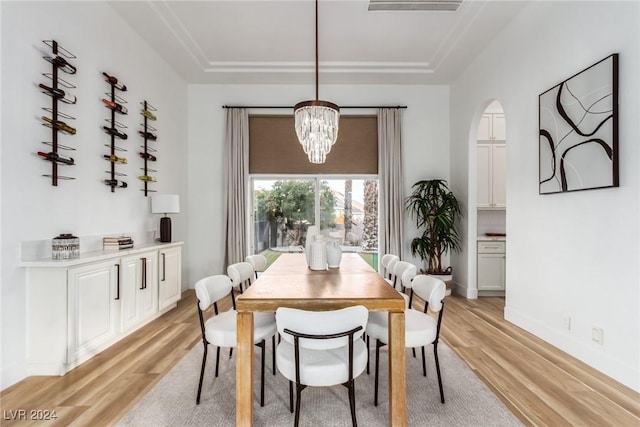 dining room with a raised ceiling, light hardwood / wood-style flooring, and a chandelier