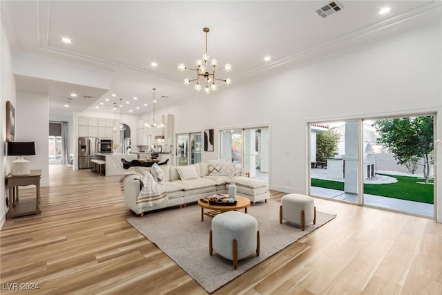 living room featuring a high ceiling, a chandelier, light hardwood / wood-style floors, and crown molding