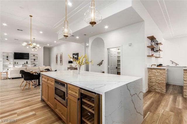 kitchen with beverage cooler, light hardwood / wood-style floors, light stone counters, stainless steel microwave, and decorative light fixtures