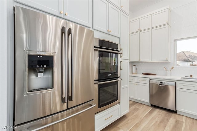 kitchen with stainless steel appliances, white cabinets, tasteful backsplash, and light hardwood / wood-style flooring