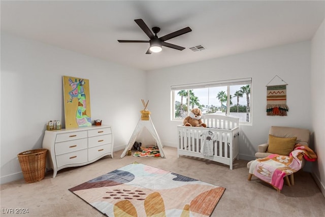 carpeted bedroom featuring a crib and ceiling fan