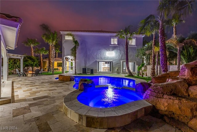 pool at dusk with a pergola, an in ground hot tub, and a patio area