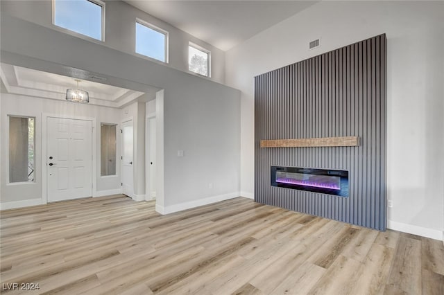 unfurnished living room with a notable chandelier, light hardwood / wood-style floors, and a tray ceiling