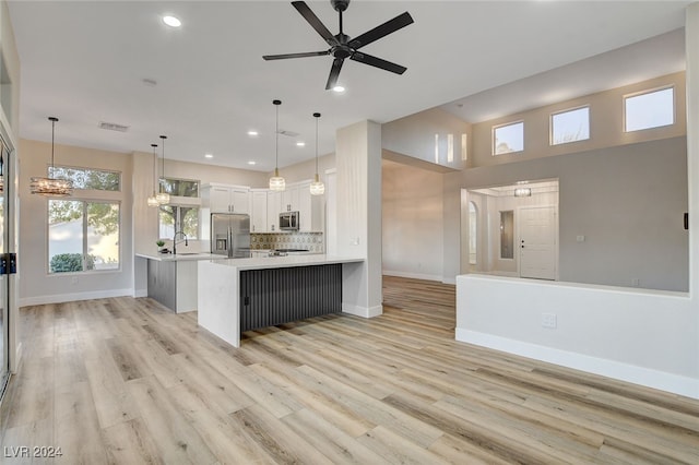 kitchen with kitchen peninsula, light hardwood / wood-style flooring, appliances with stainless steel finishes, decorative light fixtures, and white cabinetry