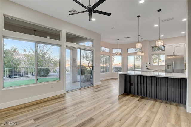 kitchen with white cabinets, stainless steel refrigerator with ice dispenser, light wood-type flooring, and a healthy amount of sunlight