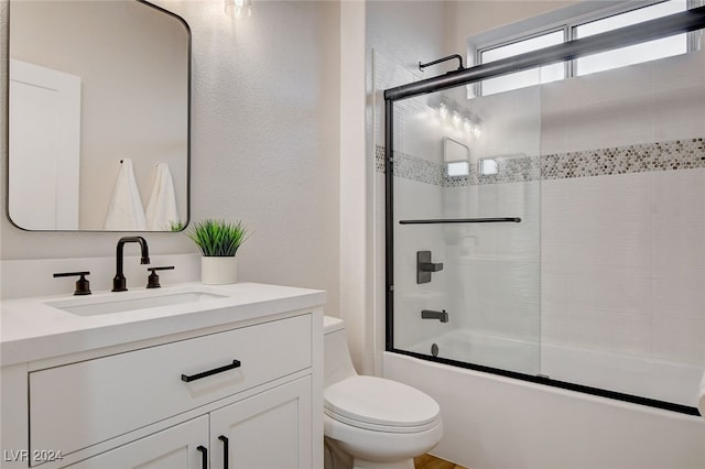 full bathroom with combined bath / shower with glass door, vanity, and toilet