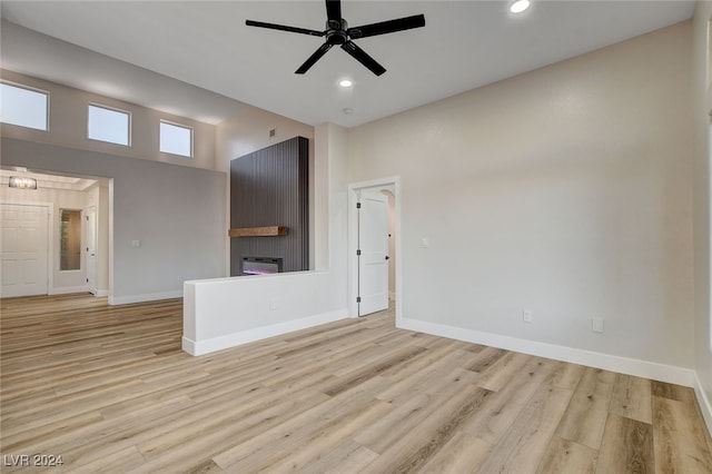 unfurnished living room with ceiling fan, a fireplace, a high ceiling, and light wood-type flooring