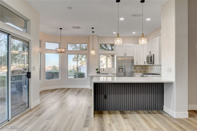 kitchen with pendant lighting, white cabinetry, stainless steel appliances, and light hardwood / wood-style flooring