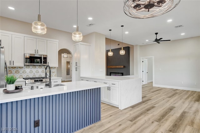 kitchen with stainless steel appliances, ceiling fan, a kitchen island with sink, decorative light fixtures, and light hardwood / wood-style flooring