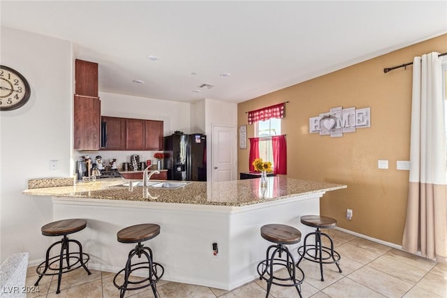 kitchen with kitchen peninsula, a breakfast bar, black fridge with ice dispenser, sink, and light tile patterned flooring