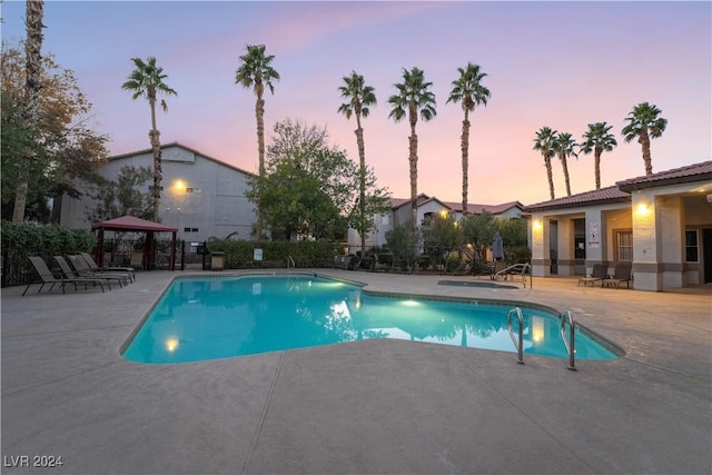 pool at dusk with a gazebo and a patio