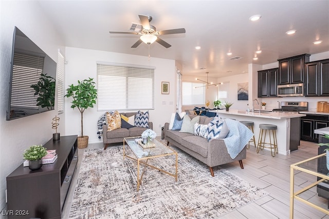 living room with ceiling fan with notable chandelier, sink, and light hardwood / wood-style flooring