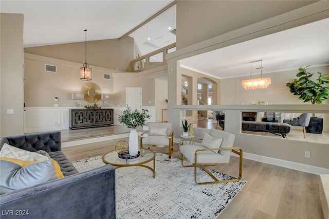 living room with ornamental molding, light hardwood / wood-style floors, lofted ceiling, and a notable chandelier