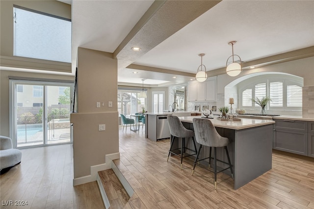 kitchen with gray cabinets, a wealth of natural light, an island with sink, and hanging light fixtures