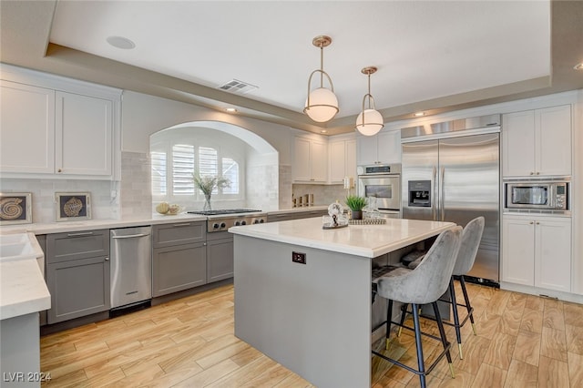 kitchen with built in appliances, a kitchen island, hanging light fixtures, and light wood-type flooring