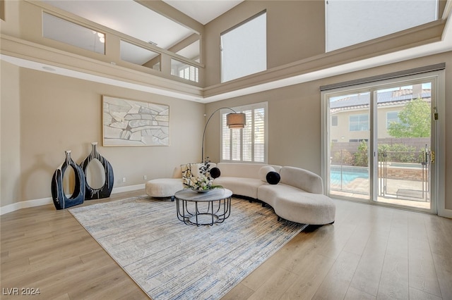 living area featuring beamed ceiling, a towering ceiling, light wood-type flooring, and a wealth of natural light