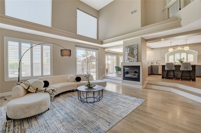 living room with light wood-type flooring, a towering ceiling, and a wealth of natural light