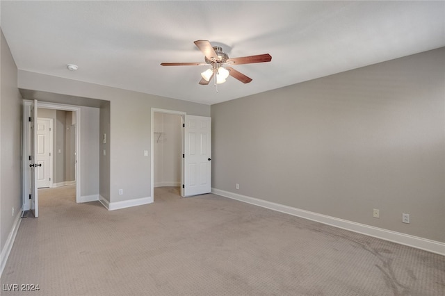 unfurnished bedroom with ceiling fan, a closet, light colored carpet, and a spacious closet