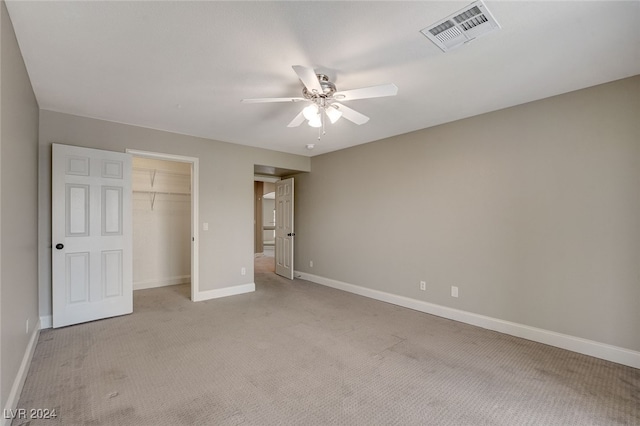 unfurnished bedroom with a closet, light colored carpet, a spacious closet, and ceiling fan