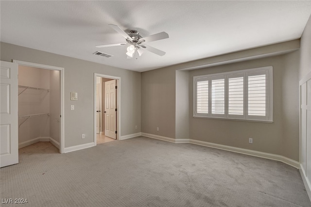 unfurnished bedroom featuring ceiling fan, a closet, light carpet, and a spacious closet