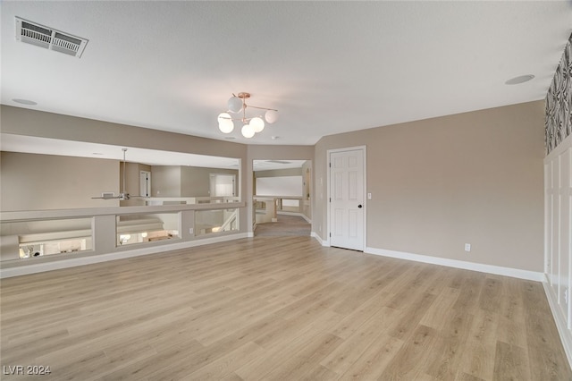 unfurnished living room with light hardwood / wood-style flooring, a chandelier, and a textured ceiling