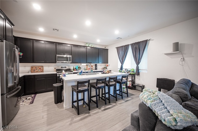 kitchen with a center island with sink, a breakfast bar, light hardwood / wood-style floors, and appliances with stainless steel finishes