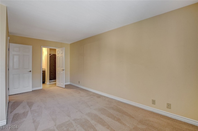 spare room featuring light colored carpet and baseboards