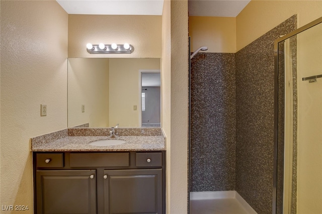 bathroom with a textured wall, a shower stall, and vanity