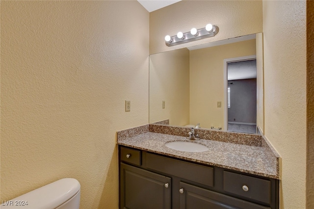 half bathroom featuring a textured wall, vanity, and toilet